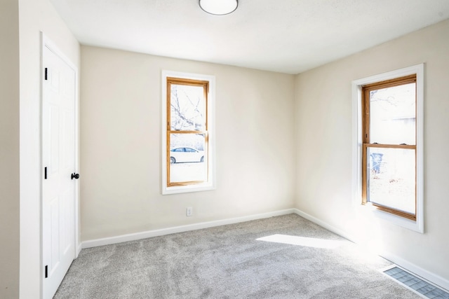 carpeted spare room with a healthy amount of sunlight, visible vents, and baseboards