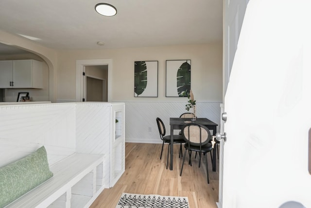 dining room with light wood finished floors, arched walkways, and wainscoting