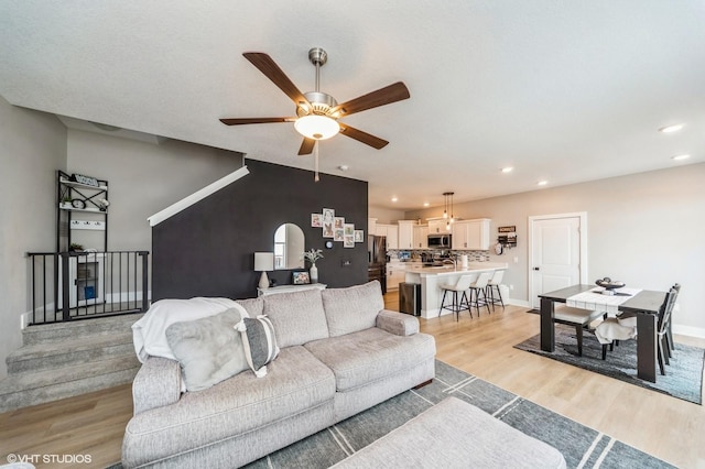 living room featuring baseboards, light wood finished floors, a ceiling fan, and recessed lighting