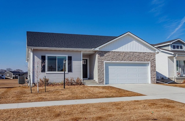 single story home featuring a shingled roof, an attached garage, central AC unit, stone siding, and driveway