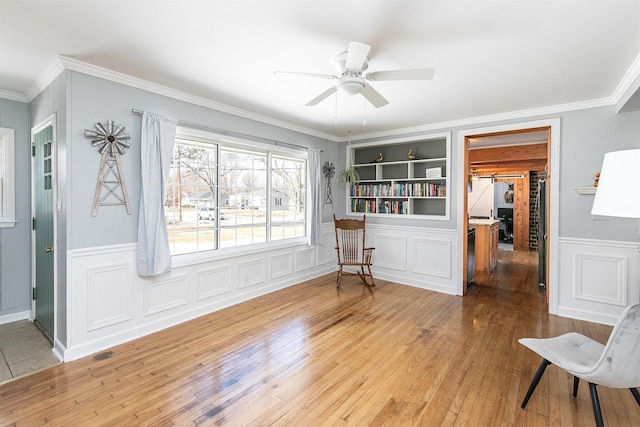 living area featuring built in shelves, ornamental molding, wainscoting, and hardwood / wood-style floors