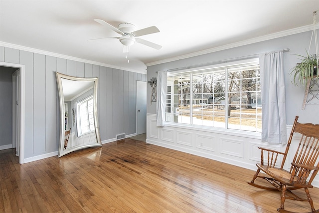 interior space with ornamental molding, light wood-type flooring, visible vents, and a ceiling fan