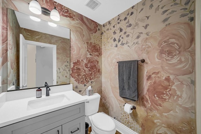 half bathroom with toilet, wallpapered walls, visible vents, and vanity