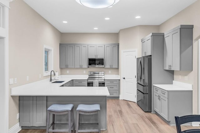 kitchen featuring gray cabinets, light wood-style flooring, appliances with stainless steel finishes, a sink, and a peninsula