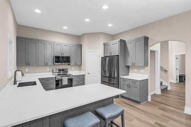 kitchen featuring arched walkways, gray cabinetry, appliances with stainless steel finishes, a sink, and a peninsula