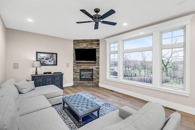 living area with a stone fireplace, wood finished floors, visible vents, and baseboards