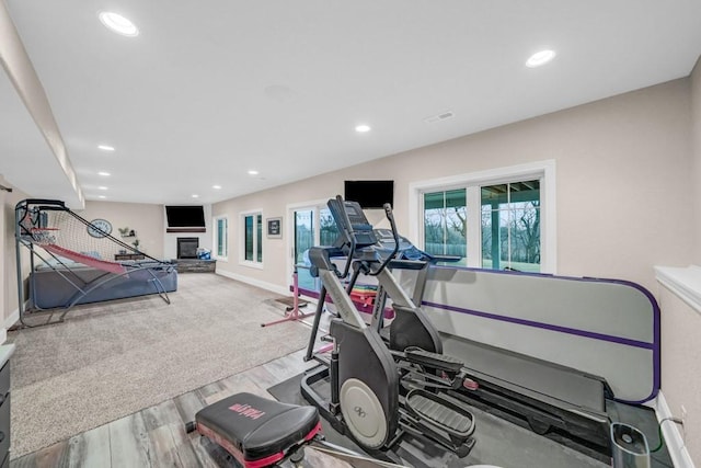 workout room with baseboards, a glass covered fireplace, wood finished floors, and recessed lighting