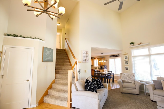 living room with baseboards, stairway, a high ceiling, and ceiling fan with notable chandelier