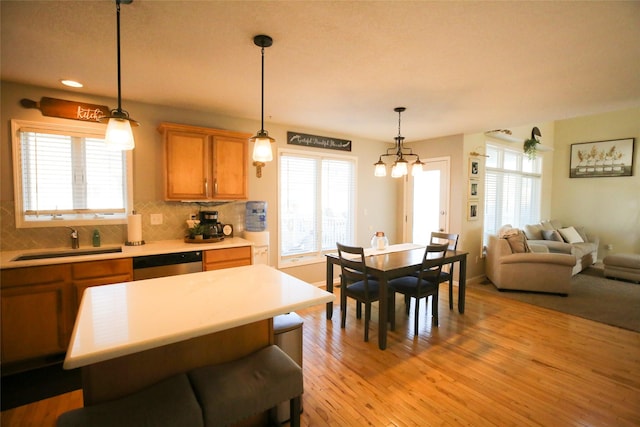 kitchen with light wood finished floors, dishwasher, a sink, light countertops, and backsplash