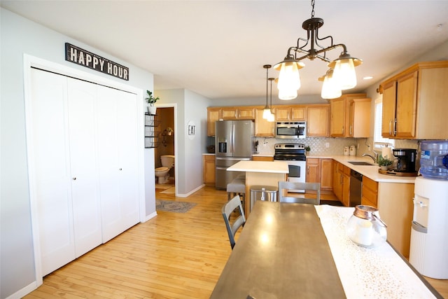 kitchen with stainless steel appliances, a sink, light countertops, light wood-type flooring, and decorative backsplash