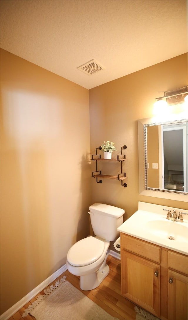 half bathroom with toilet, wood finished floors, visible vents, vanity, and baseboards