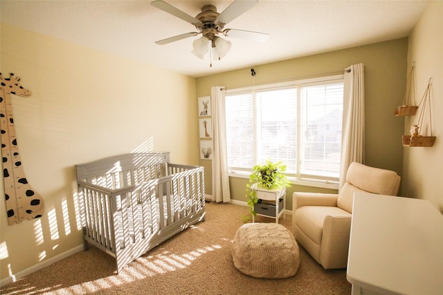 carpeted bedroom featuring a nursery area, ceiling fan, and baseboards