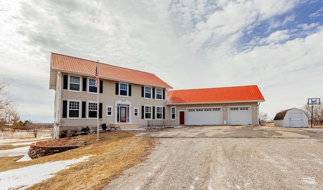 colonial home with metal roof, driveway, a shed, and a garage