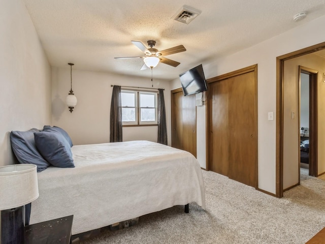 bedroom featuring a ceiling fan, carpet, visible vents, a textured ceiling, and two closets