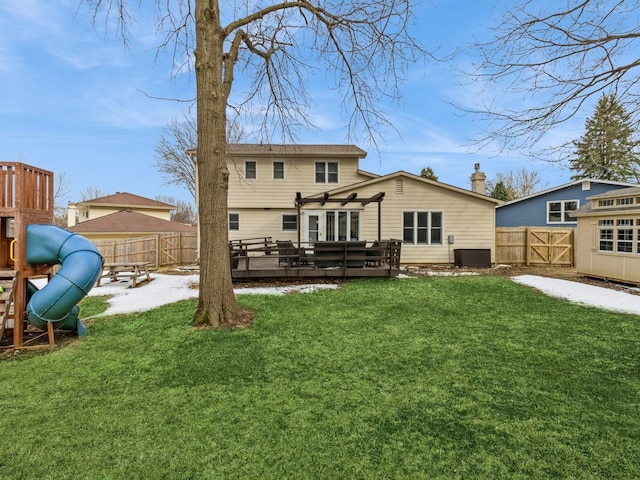 rear view of house with a lawn, a fenced backyard, a playground, a wooden deck, and a chimney