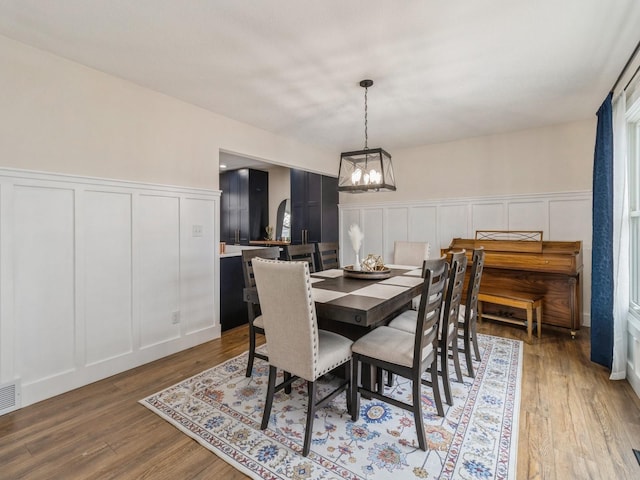 dining space featuring a decorative wall, a notable chandelier, light wood-style floors, and visible vents