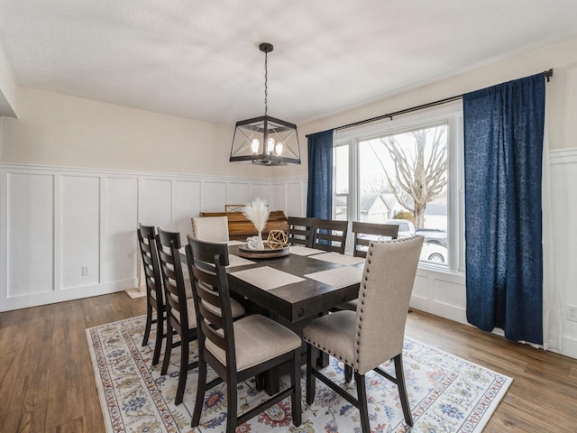 dining space featuring a notable chandelier, a decorative wall, and wood finished floors