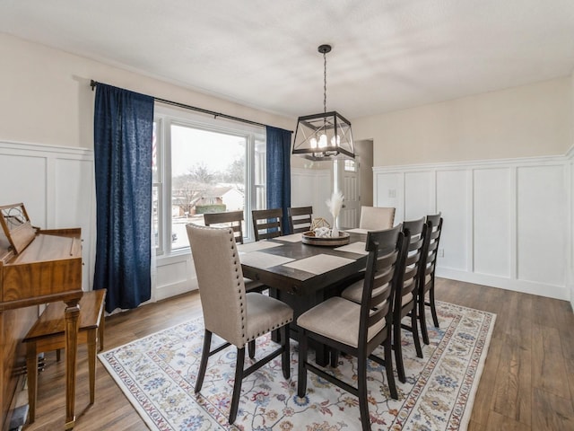 dining area featuring a decorative wall, a notable chandelier, wood finished floors, and wainscoting