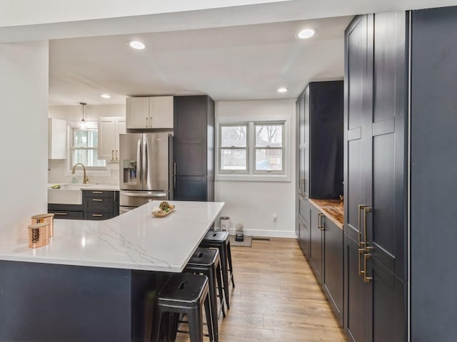 kitchen with light wood-style flooring, a kitchen breakfast bar, tasteful backsplash, stainless steel fridge with ice dispenser, and light stone countertops