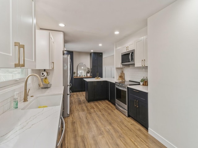 kitchen featuring light stone counters, a sink, appliances with stainless steel finishes, light wood-type flooring, and backsplash