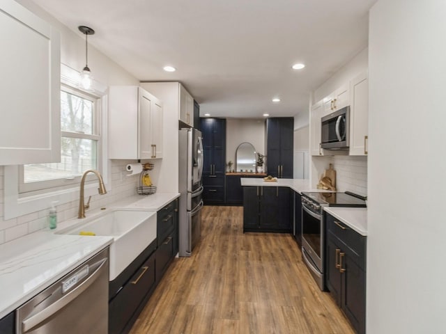 kitchen featuring light stone counters, light wood finished floors, a sink, stainless steel appliances, and white cabinets