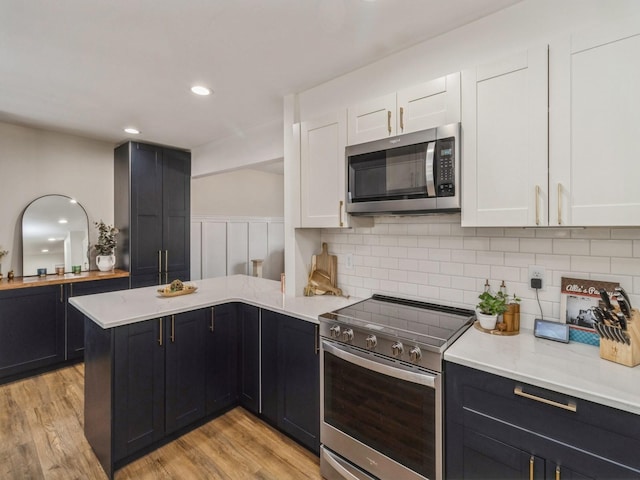 kitchen with white cabinetry, a peninsula, light wood finished floors, and stainless steel appliances