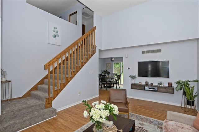 living room with visible vents, a high ceiling, wood finished floors, baseboards, and stairs