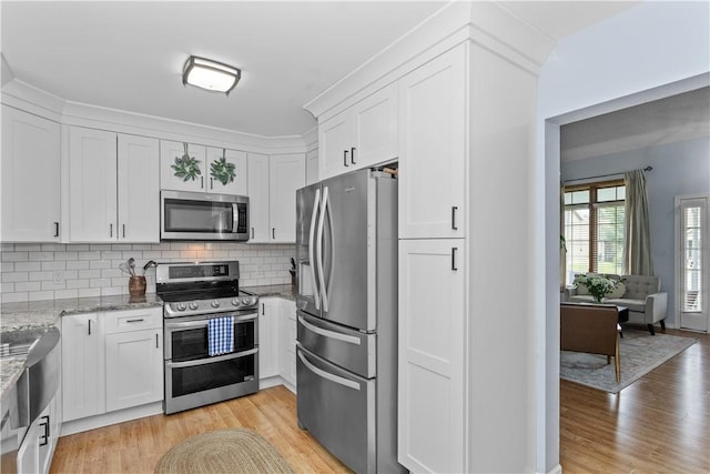 kitchen with stainless steel appliances, white cabinets, light wood-style flooring, and light stone countertops