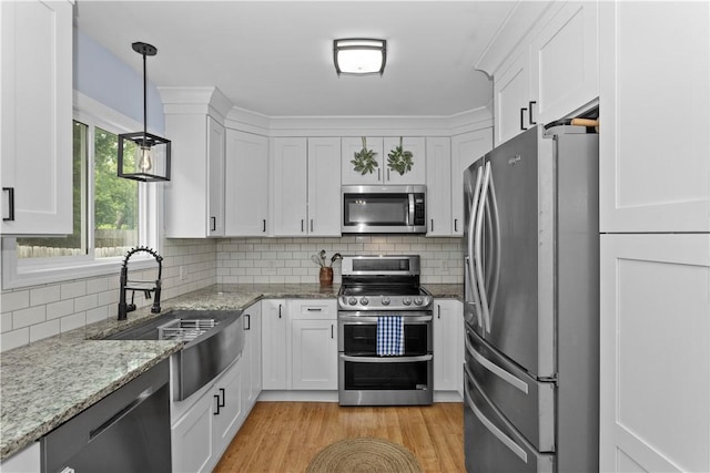 kitchen with light wood-style flooring, stainless steel appliances, a sink, white cabinets, and tasteful backsplash