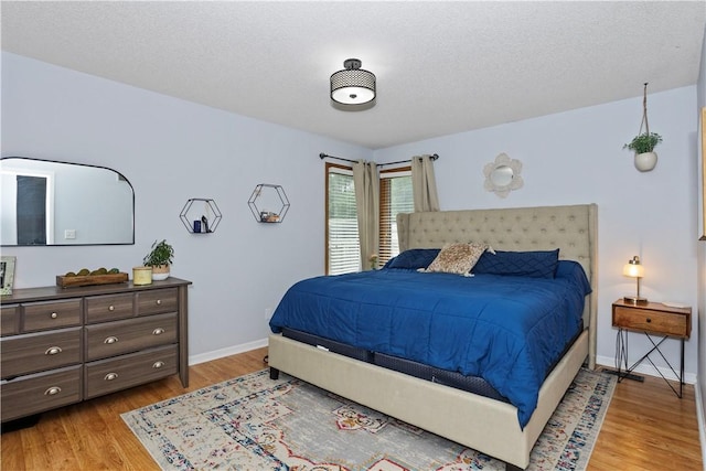 bedroom with a textured ceiling, light wood finished floors, and baseboards