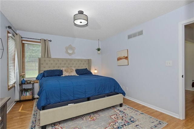 bedroom featuring a textured ceiling, wood finished floors, visible vents, and baseboards