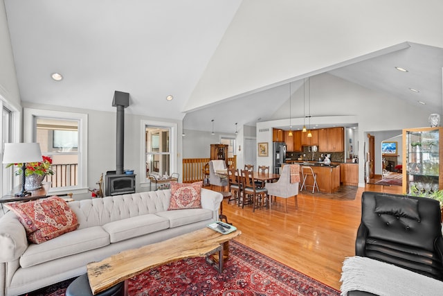 living area with high vaulted ceiling, recessed lighting, a wood stove, and light wood finished floors