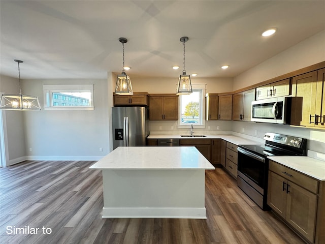 kitchen with appliances with stainless steel finishes, dark wood-type flooring, a center island, light countertops, and a sink