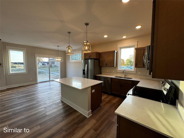 kitchen with dark wood finished floors, stainless steel appliances, hanging light fixtures, a sink, and a kitchen island