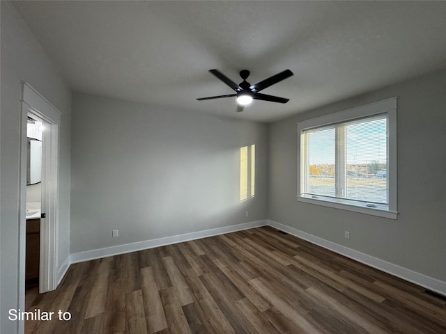 empty room with a ceiling fan, dark wood finished floors, visible vents, and baseboards