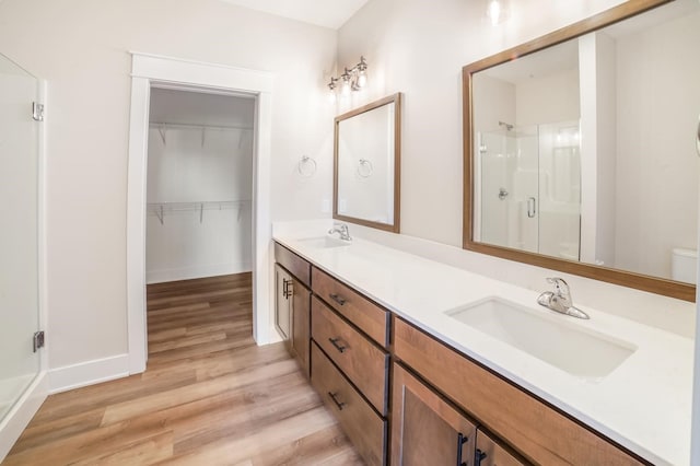 712 Academy Cir, Nevada, IA 50201 - bathroom featuring a shower stall, wood finished floors, double vanity, a spacious closet, and baseboards