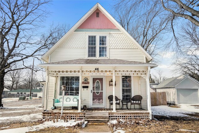 victorian-style house featuring an outbuilding, fence, covered porch, and a detached garage