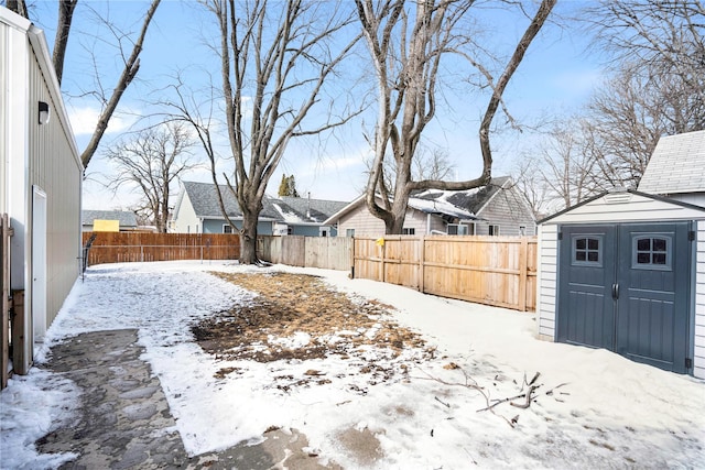 snowy yard with an outbuilding, a storage unit, a fenced backyard, and a residential view