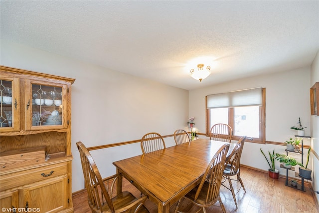 dining space with baseboards, a textured ceiling, and light wood finished floors