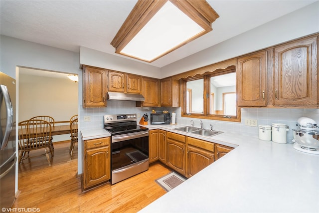 kitchen with under cabinet range hood, a sink, light countertops, appliances with stainless steel finishes, and light wood finished floors