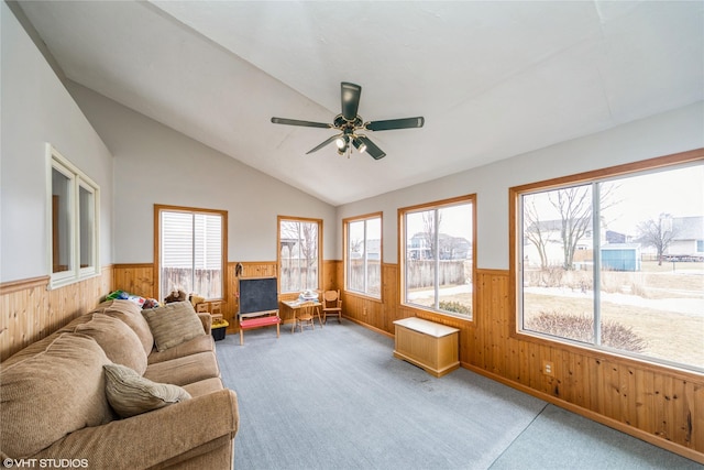 carpeted living area featuring a wainscoted wall, ceiling fan, vaulted ceiling, and wooden walls