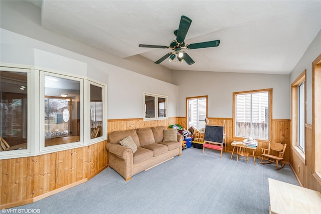 carpeted living area featuring a ceiling fan, lofted ceiling, wainscoting, and wood walls