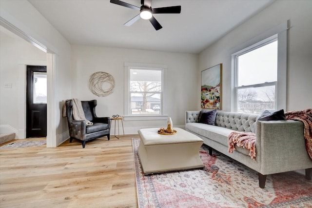 living area with a ceiling fan, light wood-type flooring, and baseboards