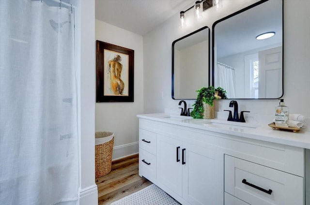 bathroom with double vanity, wood finished floors, a sink, and baseboards