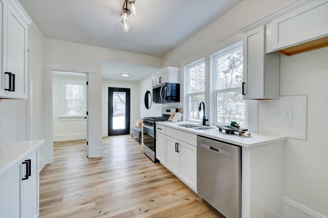 kitchen featuring stainless steel appliances, a sink, light wood-style floors, light countertops, and decorative backsplash