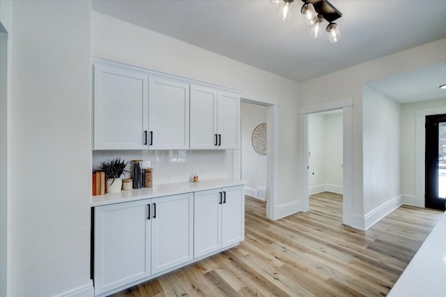 bar featuring light wood-style floors, baseboards, and backsplash