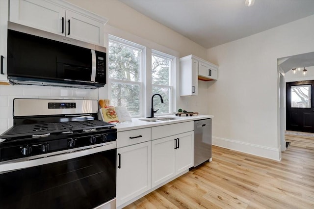 kitchen with baseboards, light wood-style flooring, appliances with stainless steel finishes, white cabinetry, and a sink