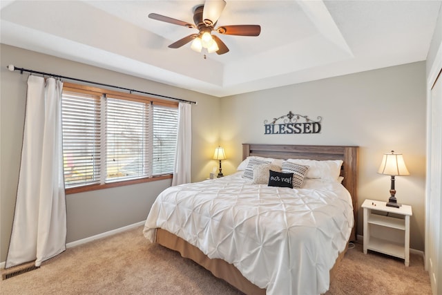 carpeted bedroom with visible vents, baseboards, a raised ceiling, and a ceiling fan