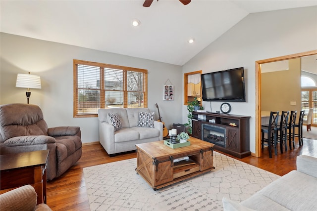 living area with lofted ceiling, recessed lighting, wood finished floors, a ceiling fan, and a glass covered fireplace