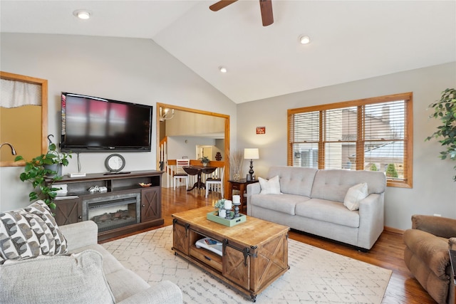 living room with a glass covered fireplace, ceiling fan, vaulted ceiling, light wood-style floors, and recessed lighting